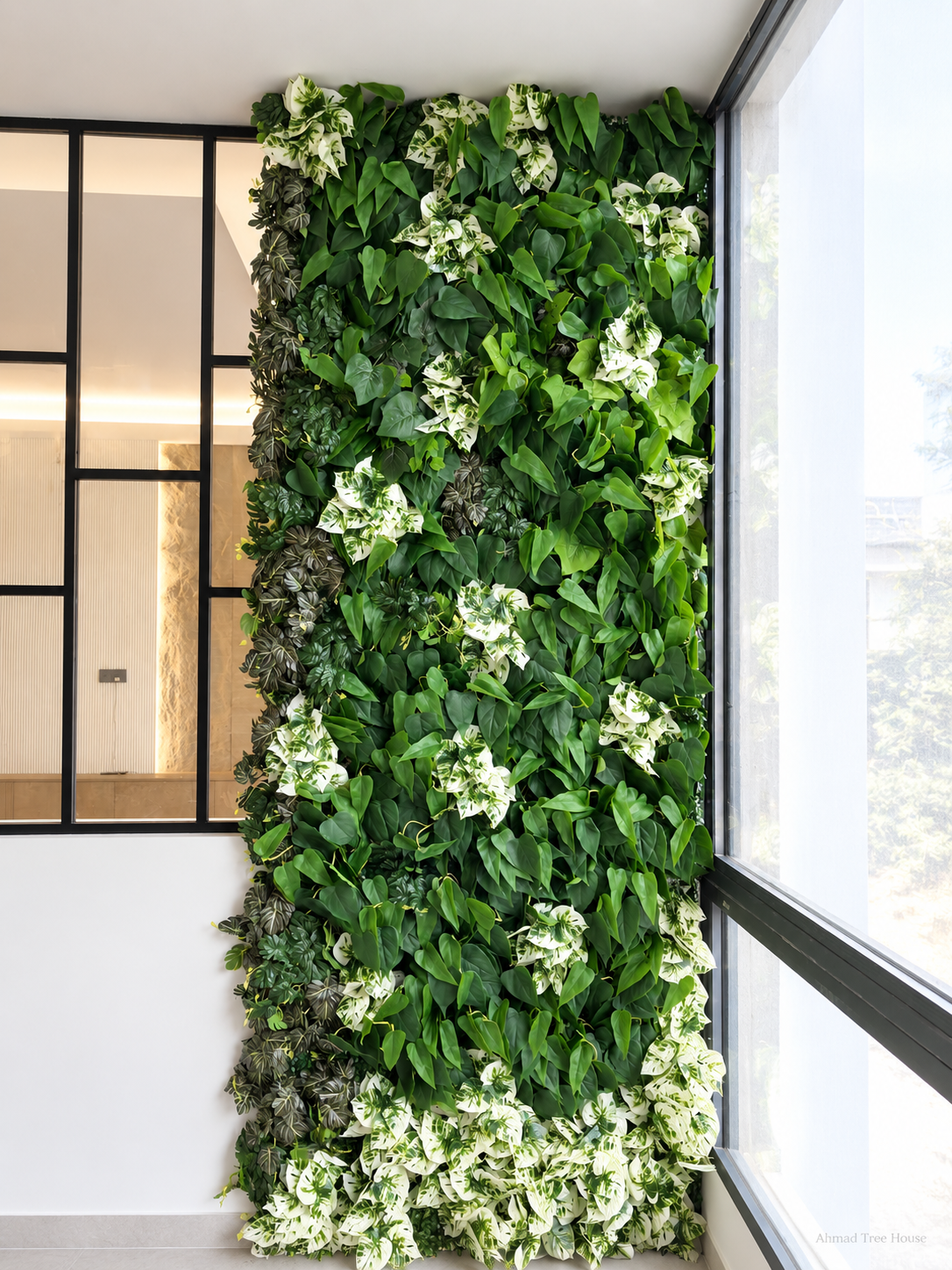Vertical mixed-leaf greenery column beside a window — Ahmad Tree House project