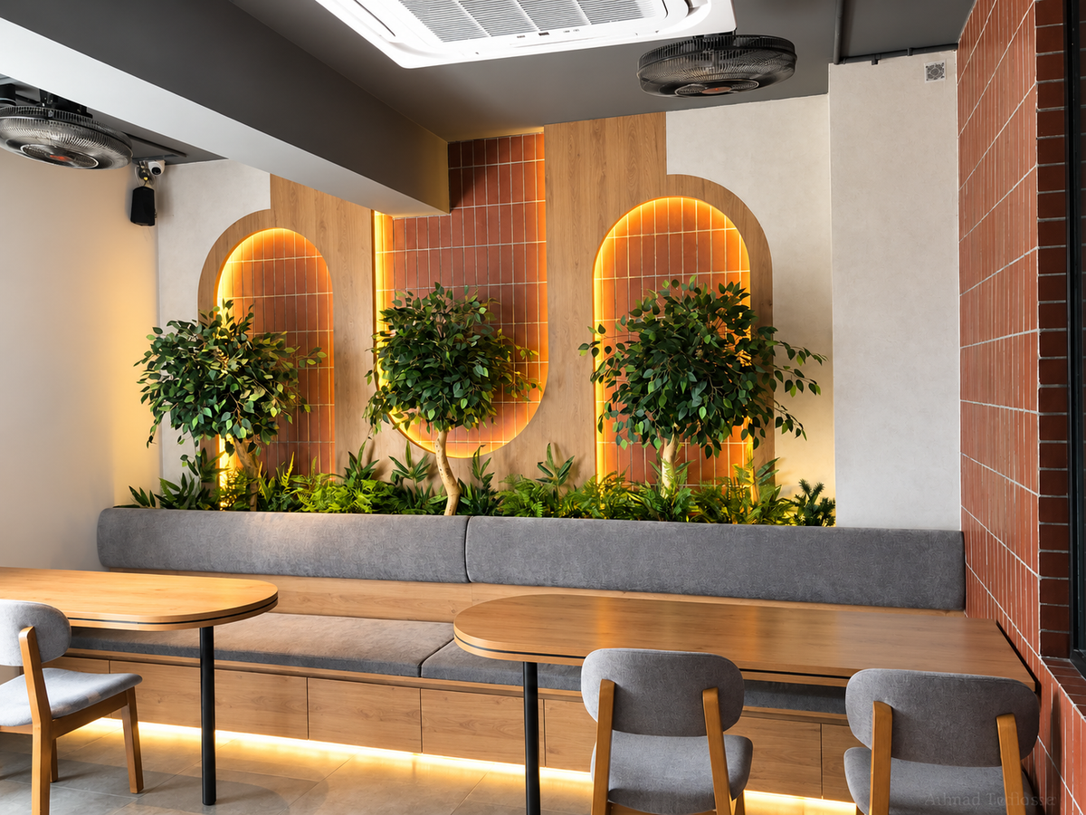 Three trees and foliage behind restaurant banquette seating with warm backlighting — Ahmad Tree House project